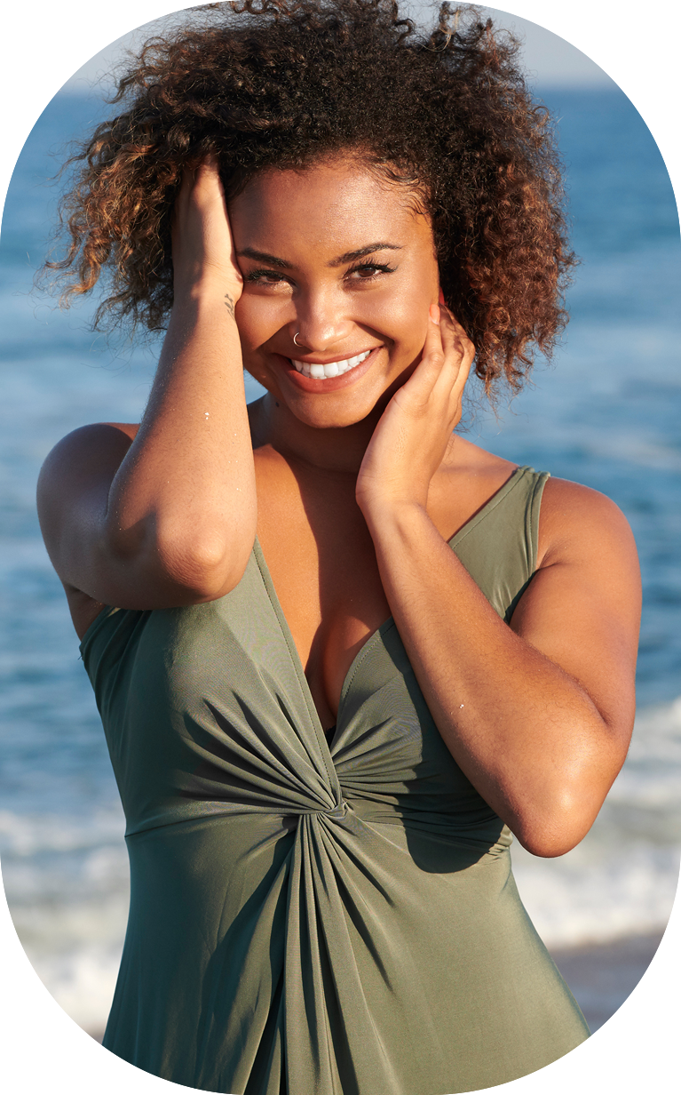Stunning young bi-racial woman in green dress on beach at sunset