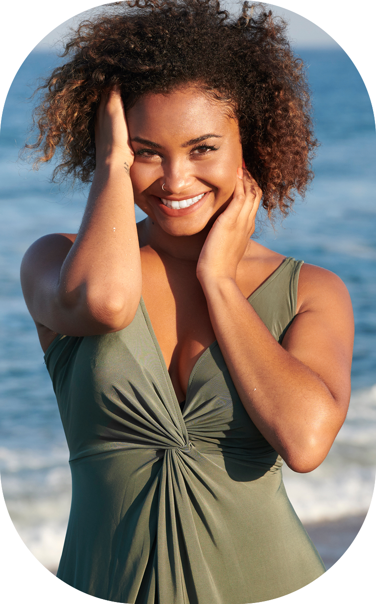 Stunning young bi-racial woman in green dress on beach at sunset