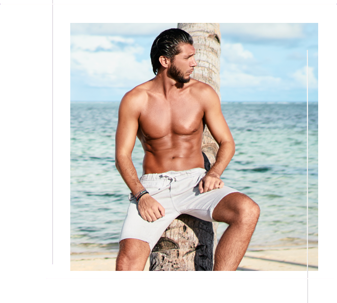 Enjoying suntan and vacation. Portrait of young bearded man leaning on coconut palm tree on the tropical beach