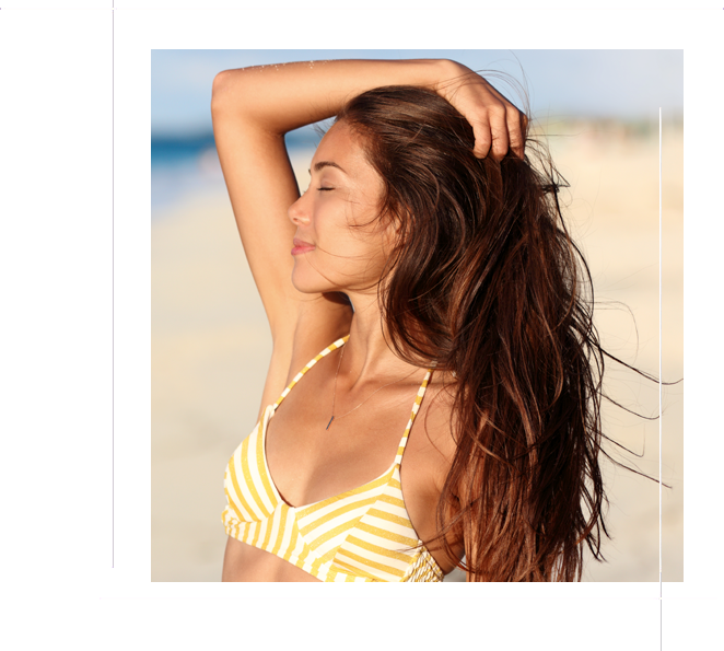 Carefree bikini woman enjoying sunset on beach. Beautiful relaxing Asian model caressing hair with closed eyes over the ocean on summer travel vacation in yellow swimsuit top in tropical destination.