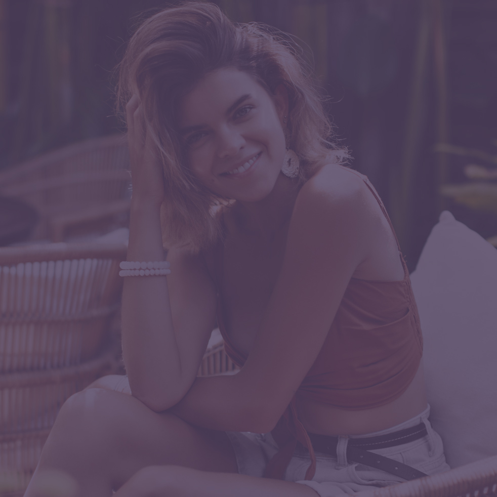 Tanned pretty girl in brown top and shorts sincerely smiles and sits in wooden chair. Happy attractive short-haired woman chilling out in tropical garden