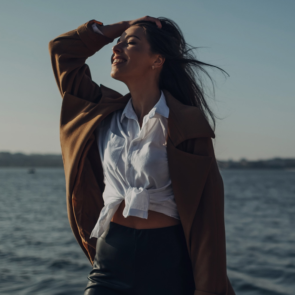 Beautiful Young Stylish Girl in Coat Walking in the Spring Beach at Sunset