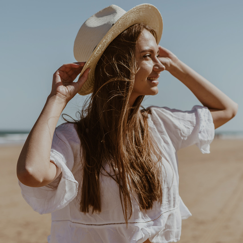 attractive european woman stands on the beach and looks into the distance, holding her hat with her hands