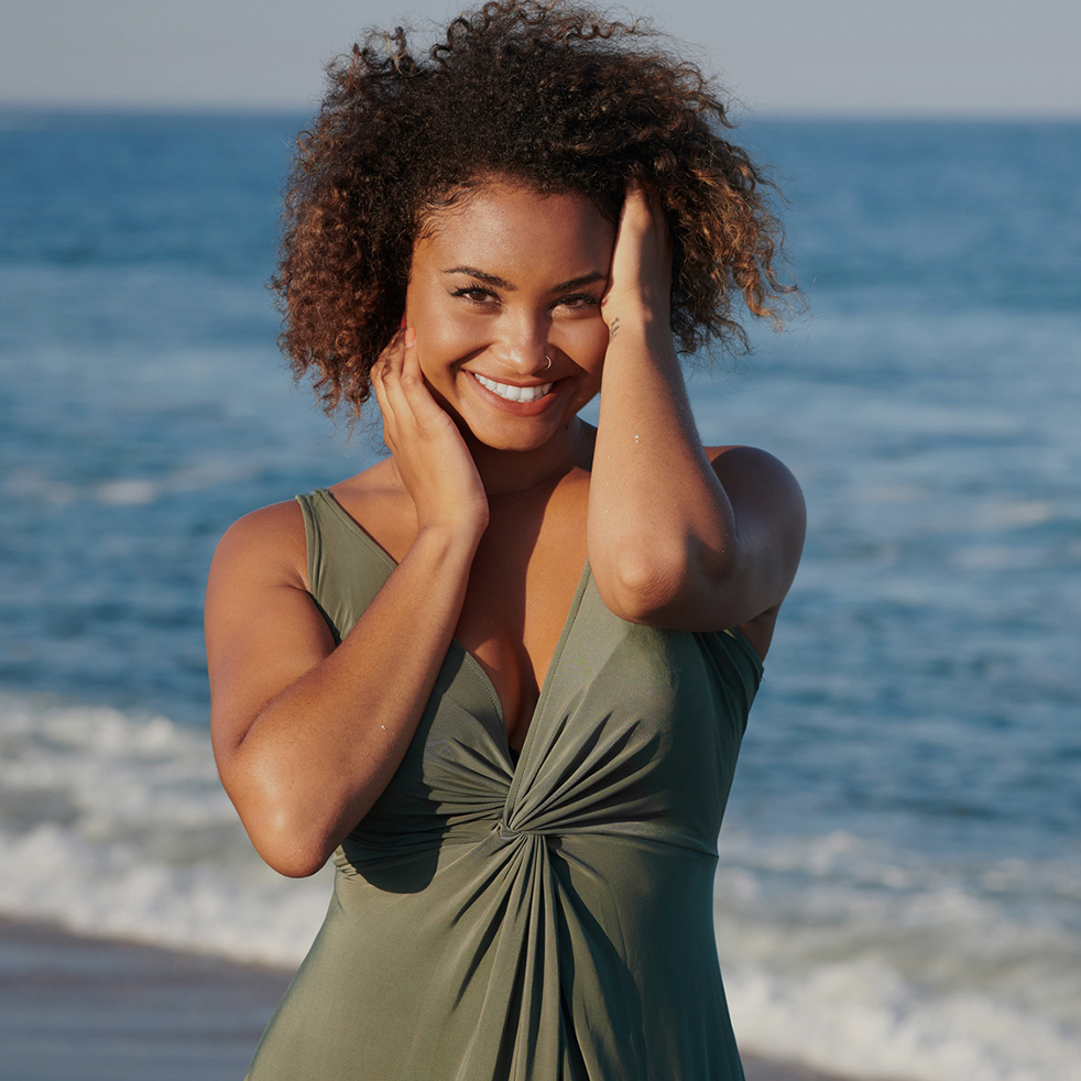 A girl in a hat at sunset near the ocean splashes water with splashes. A woman's style and fashion, relaxing on the beach, walking, with space