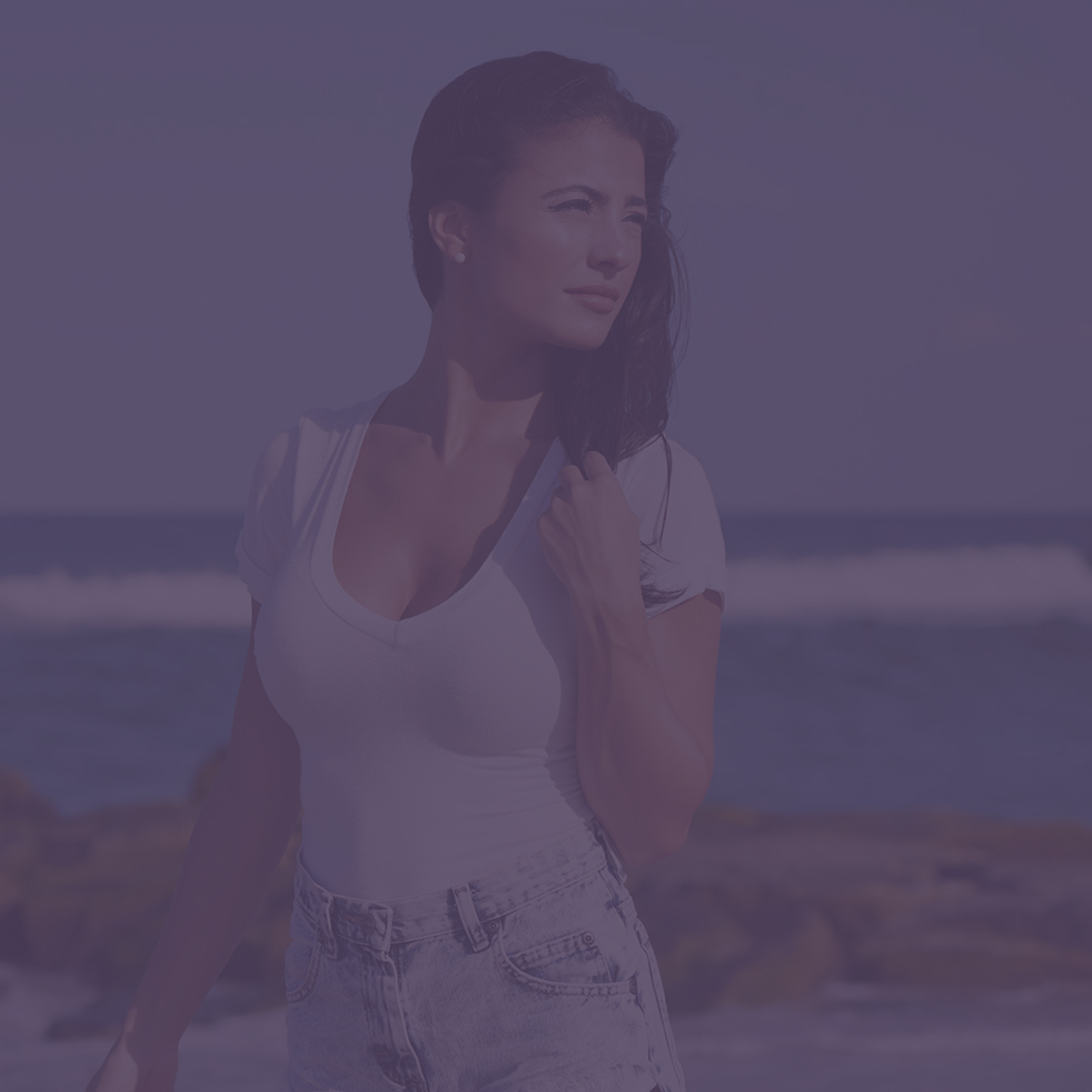 Stunning young brunette woman wearing white t-shirt and denim shorts on beach