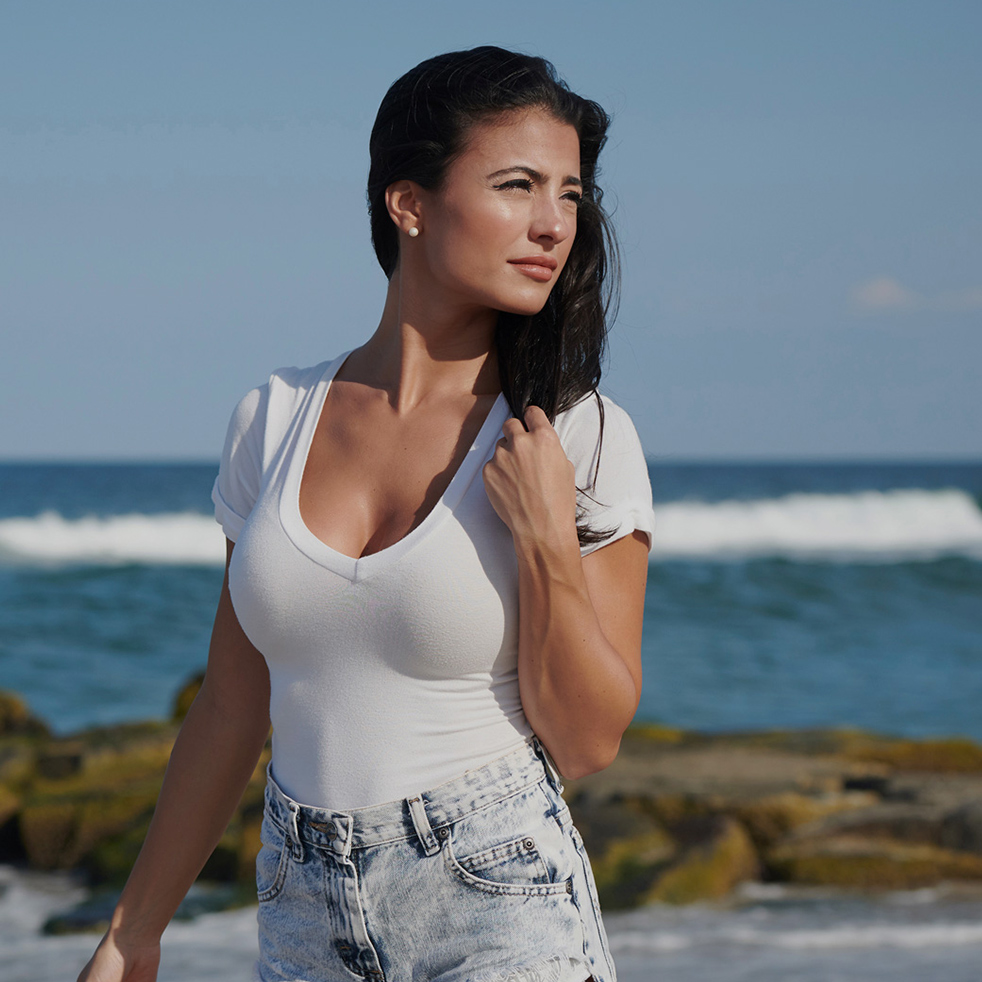 Stunning young brunette woman wearing white t-shirt and denim shorts on beach